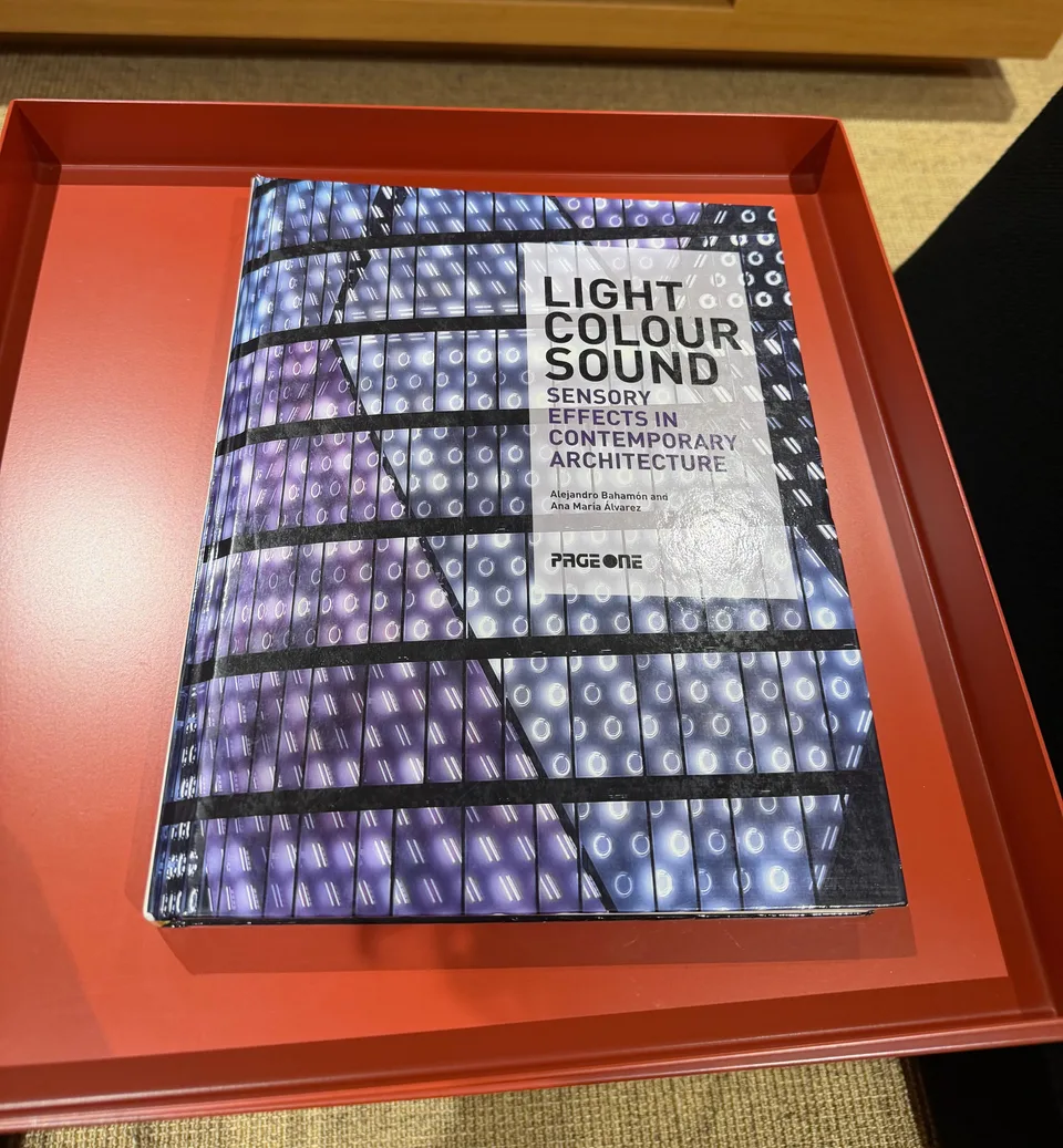 書籍『Light, Colour, Sound: Sensory Effects in Contemporary Architecture』が赤いトレイに置かれている。表紙は紫や青に光る丸い照明が並んだ建物の外壁の写真